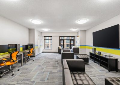 View of gaming lounge with chairs, consoles, gaming PCs, & large TV.