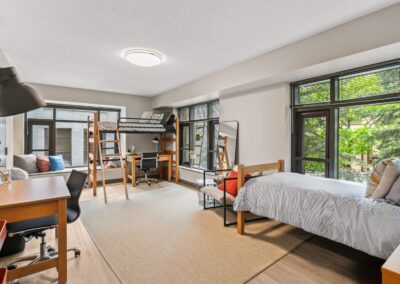 View of shared bedroom with 2 beds, desks, and chairs.